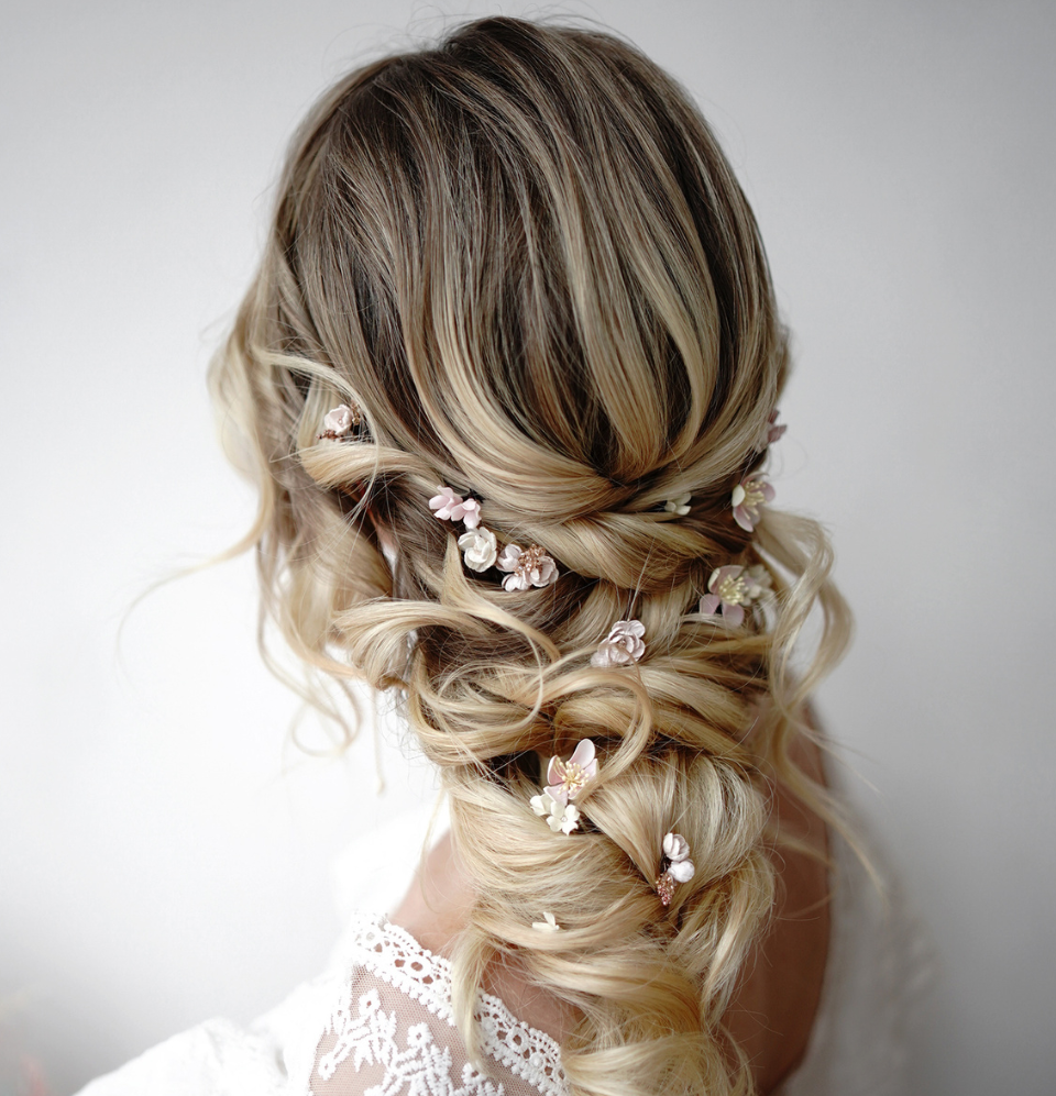 A back view of an elegant loose bridal updo with a detailed braided structure on blonde hair, featuring small and unique pink flower hair pins by @niezwykle_czesanie.