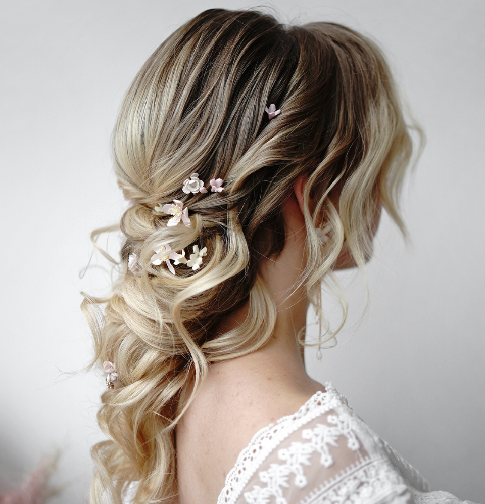 A full back profile shot of a breathtaking braided wedding hairstyle, showcasing a complete scattered display of individual blush pink cherry blossom flower hair pins across the entire styled look.
