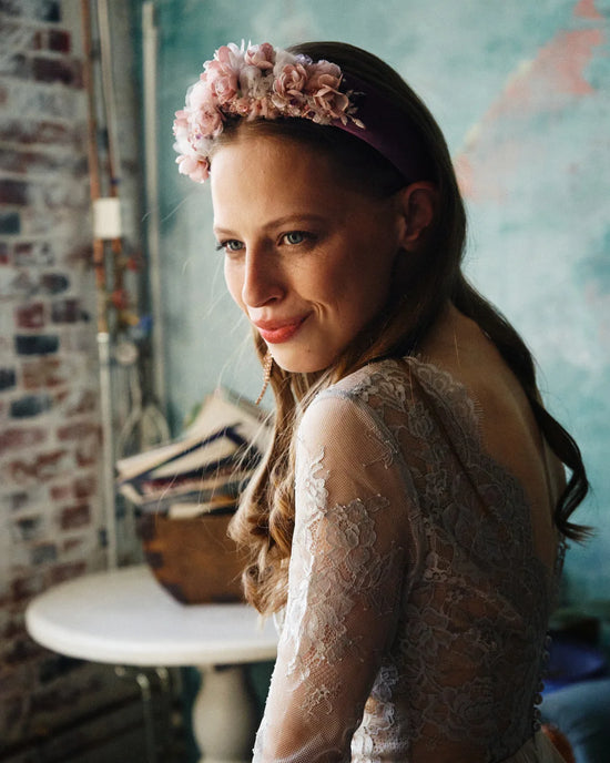 Close-up of handmade bridal headband with pink and mauve flowers, worn with loose waves and lace gown.