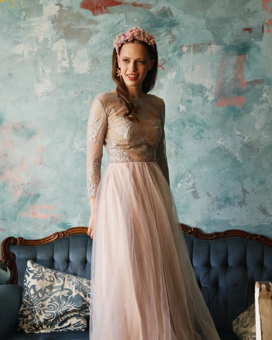 Bride wearing a mauve taupe floral bridal crown with a soft pink tulle dress, standing against a textured teal wall.