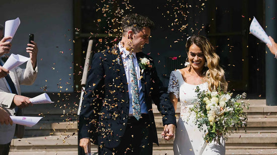 Happy bride and groom showered with golden petal confetti, featuring bespoke handcrafted bridal floral accessories by Decoflowers.