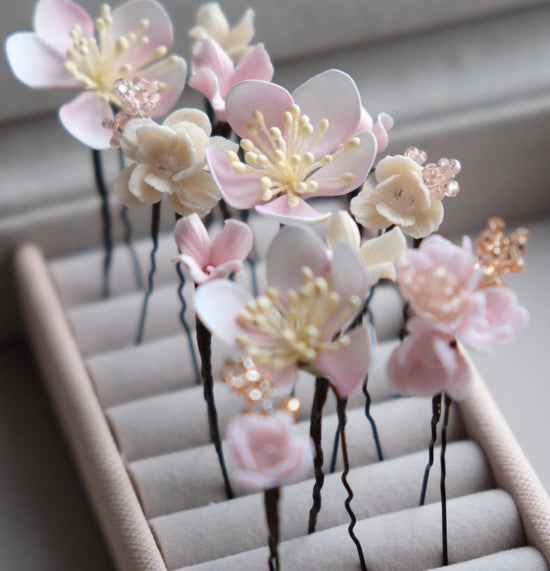A clean product photograph from above of a lined gift box holding a ten-piece collection of realistic pink cherry blossom floral hair pins, perfect for a bride&